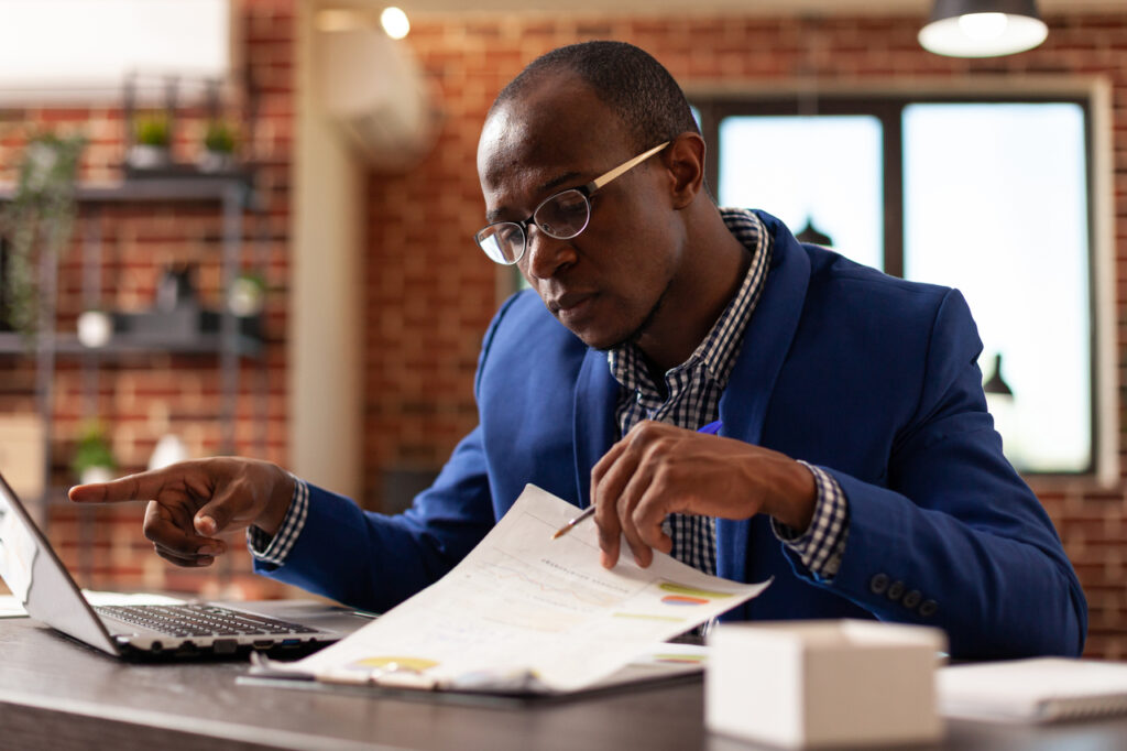 Business man analyzing papers on clipboard to plan marketing strategy with laptop